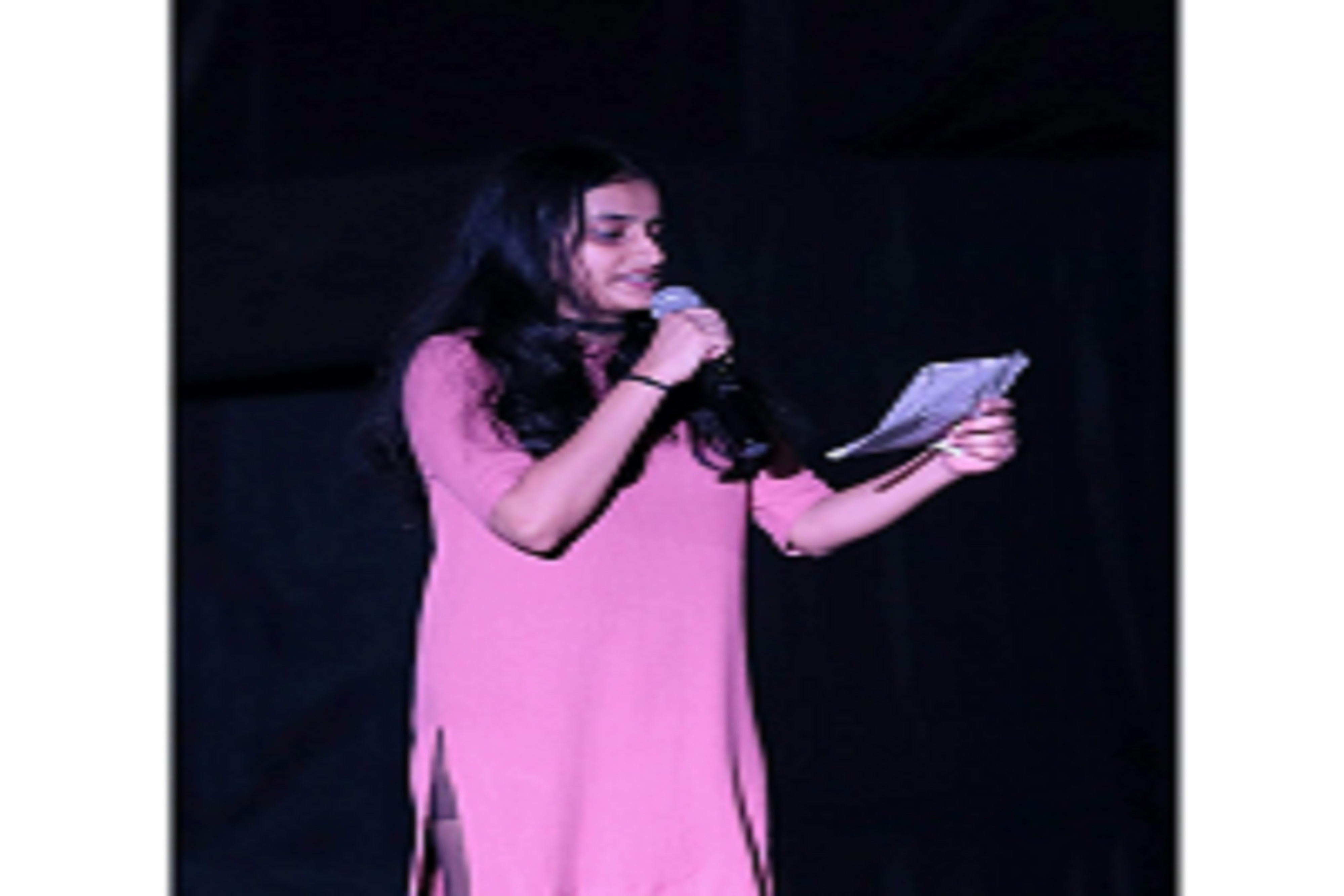 A girl reciting a poem on a stage with mic in her hand