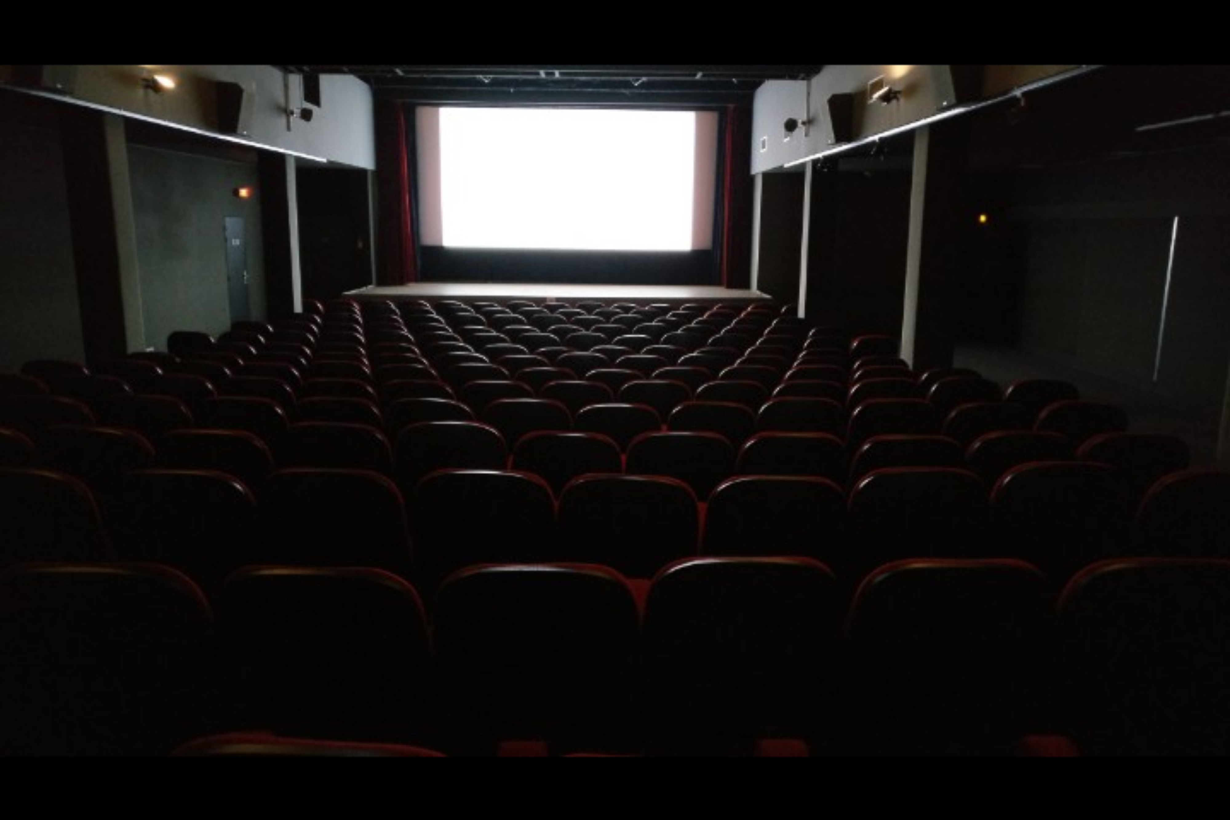 A movie being projected on the big screen of a theatre full of red empty seats.
